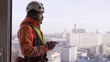 Beyaz kasklı işçi çatıda duruyor. Endüstriyel dağcı bilgi topluyor ve verileri tablete yerleştiriyor.