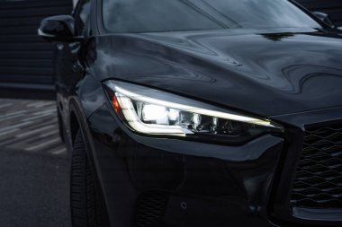 Işıklı LED farlı modern siyah bir arabanın yakın çekim detayları. Işıl ışıl vücut yansımaları, lüks ulaşım, güvenlik teknolojisi ve düşük ışıkta yakalanan özel araç tasarımı konsepti.