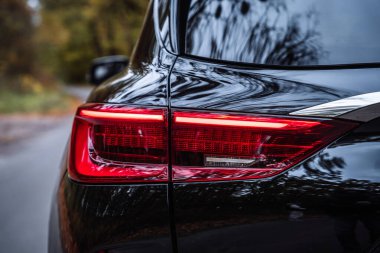 Sonbahar manzarası ile çevrili bir yolda sürerken kırmızı LED ışığı yanan arka arabanın yakın görüntüsü. Otomotiv dış detayları güvenlik ışıklandırması, görüş mesafesi ve parlak yansımalı modern araç tasarımı gösteriyor..