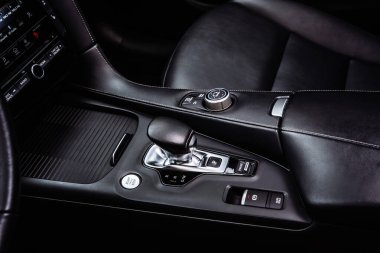 Otomatik vites seçici, sürücü modu araması ve kontrol düğmeleri olan bir araba merkezi konsolunun yakın görüntüsü. Modern araç iç ayrıntıları premium materyalleri, ergonomik tasarımı ve gelişmiş otomotiv teknolojisini vurguluyor.