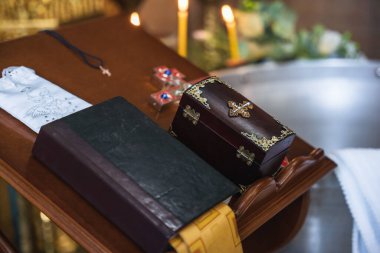 İncil 'li Ortodoks cenaze töreni detayları, tahta tabut kutusu, kilise masasında haç ve yanan mumlar. Sıcak mum ışığı, sığ alan derinliği ve yumuşak odaklanma sessiz, saygılı ve ruhani bir atmosfer yaratır..