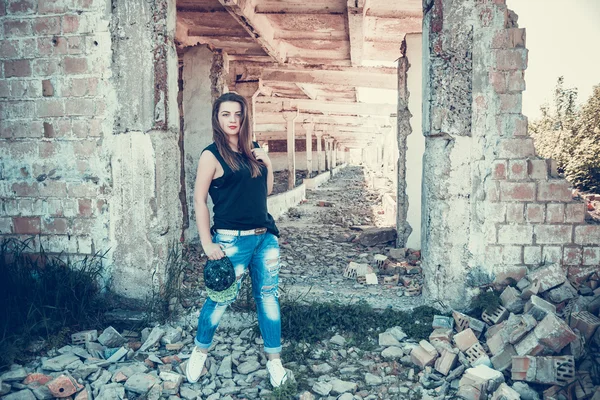 Atractiva mujer en traje de jean y taza posando en la vieja casa de fábrica en ruinas . — Foto de Stock