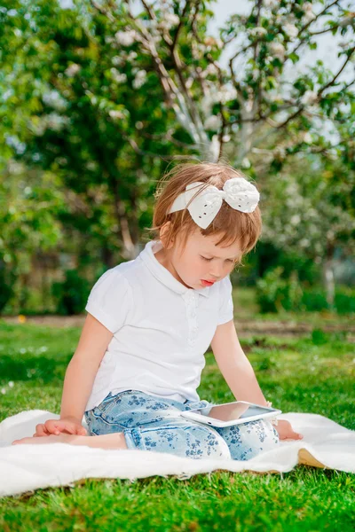 Niña vestida de polo blanco y vaqueros. Niña usando una tableta. Niña estudia con la tableta —  Fotos de Stock