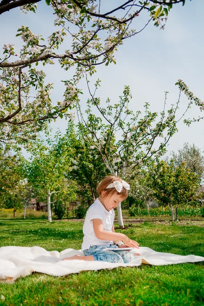 Bambina vestita di polo bianca e jeans.Girl Utilizzando una tavoletta. Ragazzina studia con la compressa — Foto Stock