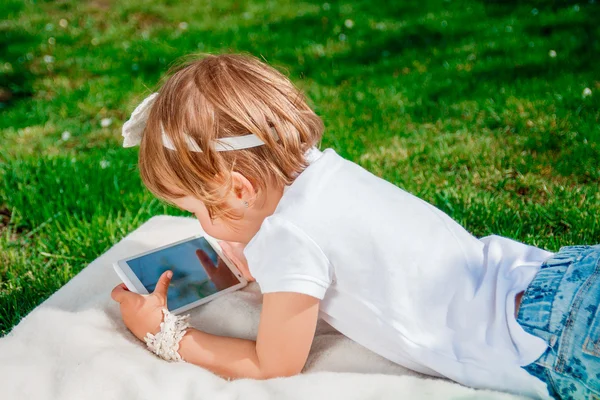Mała dziewczynka ubrana w białe polo i dżinsy. Dziewczyna przy użyciu tabletu. Mała dziewczynka badania z tabletem — Zdjęcie stockowe