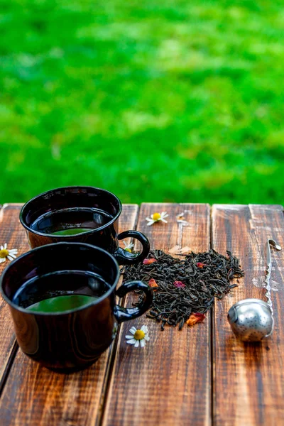 Twee kopje thee in de buurt van droge bladeren van zwarte thee maken in hart — Stockfoto