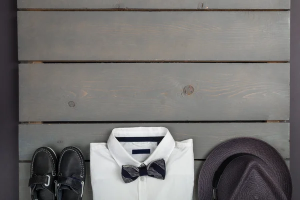 Ahşap arka plan üzerinde erkek kıyafeti. Çocuk moda giyim. Gri fedora, beyaz gömlek, siyah papyon ve tekne ayakkabı çocuk için. Üstten Görünüm. Uzay kopyalayın. Çerçeve