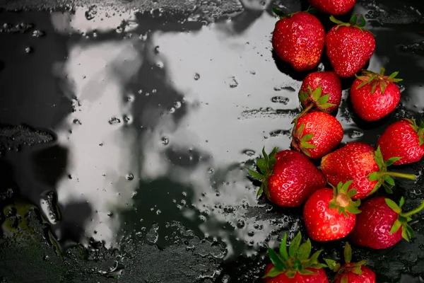 Whole strawberries on black background with water drops. Wet . Frame, copy space. Top view.