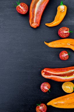 Yarım kırmızı ve sarı biber yeşil dal kiraz domates üzerinde siyah artalanları yakınındaki karışık. Üstten Görünüm. Çerçeve. Kopya alanı.