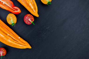 Yarım kırmızı ve sarı biber yeşil dal kiraz domates üzerinde siyah artalanları yakınındaki karışık. Üstten Görünüm. Çerçeve. Kopya alanı.