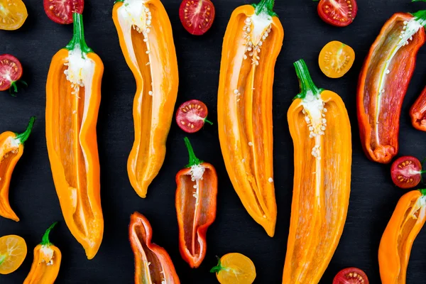 Yarım kırmızı ve sarı biber yeşil dal kiraz domates üzerinde siyah artalanları yakınındaki karışık. Üstten Görünüm.