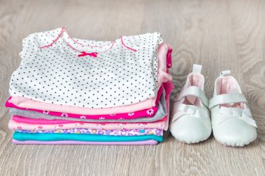 Üzerinde gri ahşap arka plan ayakkabı ile katlanmış pembe ve beyaz bodysuit. yeni doğmuş kız için bebek bezi. Bebek kıyafetleri yığını. Çocuk kıyafeti. Yakın çekim.