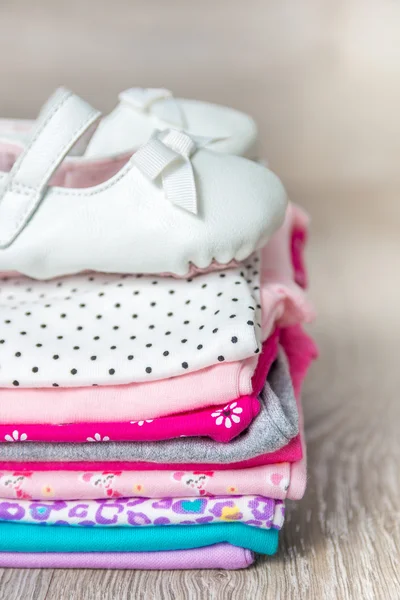 Carrocería plegada de color rosa y blanco con zapatos sobre fondo de madera gris. pañal para niña recién nacida. Montón de ropa infantil. Traje de niño. Copiar espacio . — Foto de Stock