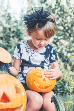 Cadılar Bayramı. Çocuk siyah ile jack-o-fener el, oyun ya da şeker giyimli. Ahşap açık havada kabak üzerinde seyir küçük kız. Tonda fotoğraf.