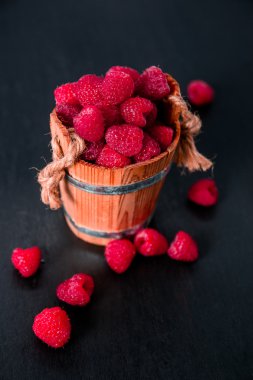 Siyah ahşap zemin üzerine bir sepet içinde kırmızı ahududu. Yakın çekim.