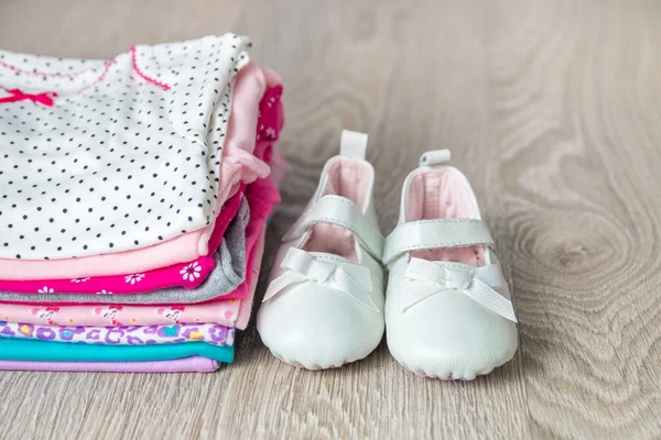 Διπλωμένο ροζ και λευκό κορμάκι με παπούτσια σε ξύλινα φόντο είναι γκρι. πάνα για νεογέννητο κοριτσάκι. Στοίβα της βρεφικής ένδυσης. Στολή του παιδιού. Χώρο αντίγραφο. — Φωτογραφία Αρχείου