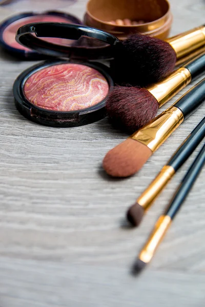 Set of decorative cosmetics and brushes on grey wooden background. Various browns makeup products. Top view, frame. Copy space. — Stock Photo, Image