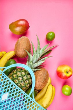 Pembe arka planda organik egzotik meyvelerle marketten alışveriş torbası. Yeniden kullanılabilir bir alışveriş çantasından dökülen taze tropikal meyve çeşitleri. Sağlıklı beslenme ve gıda kavramı. Boşluğu kopyala.
