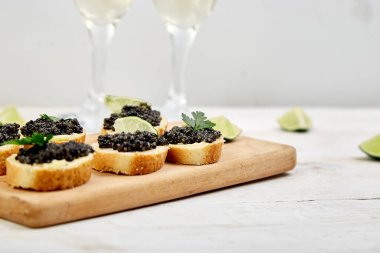 Siyah havyarlı sandviç. Tahta kasede siyah havyar, beyaz arka planda sandviç ve şampanya fotokopi alanı.