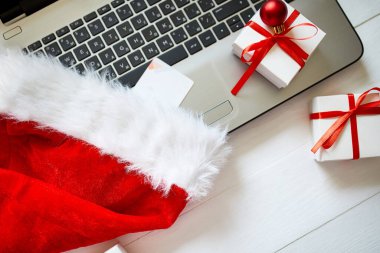 Evde yeni yıl ve Noel alışverişi, karantina konsepti, not defteri, kredi kartı, Noel Baba şapkası ve hediye kutusu beyaz ahşap arka plan, üst manzara, kopyalama alanı.