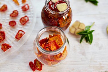 Ev yapımı güneşte kurutulmuş domatesler, beyaz ahşap zemin üzerinde cam bir kavanozda zeytinyağında sarımsak. Üst Manzara. Mutfak için yazdır