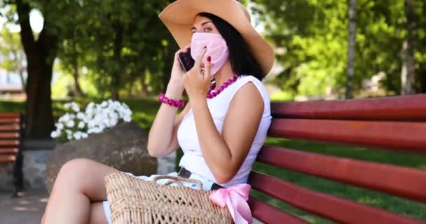 Kvinna i skyddsmask, i parken utomhus, talar på en mobil — Stockvideo