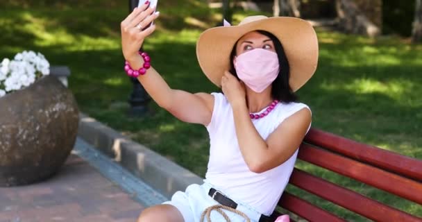 Blogger γυναίκα σε ψάθινο καπέλο με προστατευτική μάσκα, στο υπαίθριο πάρκο, να λάβει selfie — Αρχείο Βίντεο