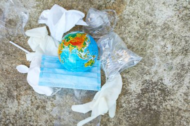 Yolun arka planında dağınık bir çöp yığınının içindeki bir küre dağınık plastik, koruyucu maske, eldiven, koronavirüs salgını sırasında atıklar..