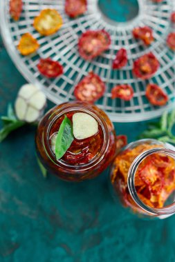 Ev yapımı güneşte kurutulmuş domatesler, zeytinyağında sarımsak koyu yeşil arka planda cam bir kavanozda. Üst Manzara. Mutfak için yazdır