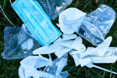 Yeşil çimenlerin üzerine saçılmış çöp yığını dağınık plastik, koruyucu maske, eldiven, koronavirüs salgını sırasında atık, dünyayı kurtarın..