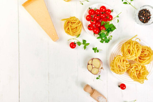 Ingredients for cooking pasta - tagliatelle, tomato, garlic, basil, parmesan cheese on white wooden background flat lay, top view, frame, copy space, Italian food concept.