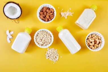 Alternatif tür vejetaryen süt şişeleri sarı arka planda, çeşitli vegan bitkiler süt ve malzemeler, süt içermeyen süt, alternatif süt, düz, fotokopi alanı ile üst görünüm