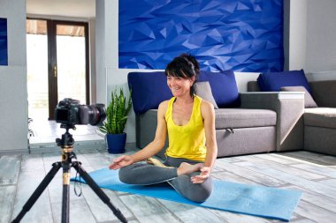 Spor kıyafetleri içinde zayıf vücutlu blogger son sınıf öğrencisi kadın evde yoga yapıyor. Fitness blogu, video dersi, çevrimiçi eğitim kameradan yoga dersi kaydı. Coronavirus karantinası, evde kalın..