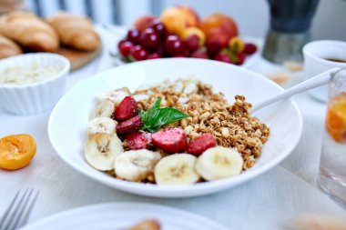 Sağlıklı kahvaltı kasesi, taze tahıl gevreği yoğurt meyveli müsli ve kahve çilek, beyaz masada muz, kopyalama alanı. Temiz yemek, detoks, diyet, vejetaryen gıda konsepti.
