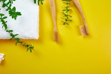 Bambu diş fırçaları ve havluyla kulak çubukları, ve sarı kağıtta yeşil yapraklar, çevre dostu, sıfır atık kişisel hijyen ürünleri, diş bakımı konsepti