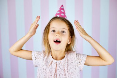 Küçük güzel bir kız pembe bir şapka takıyor pembe çizgili arka planda mutlu bir yüzle gülümsüyor. Mutlu yıllar..