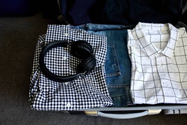 Evde sıradan erkek eşyalarıyla bavul hazırlamak. Kotlar, gömlekler, kulaklıklar seyahat, seyahat, tatil için bavullar. Boşluğu kopyala.