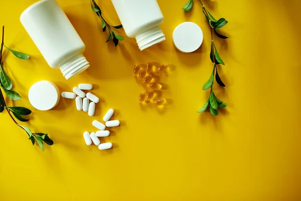 Flat lay of pills, fish oil, vitamins with green leavws on yellow background, Healthcare concept, healthy food, supplements for healthy good life, Immune booster, hard light, trend.