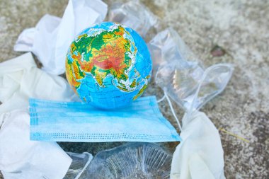 Yolun arka planında dağınık bir çöp yığınının içindeki bir küre dağınık plastik, koruyucu maske, eldiven, koronavirüs salgını sırasında atıklar..