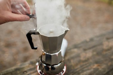 Gezgin adam, gaz ocağında metal gayzer kahve makinesiyle adım adım kamp kahvesi yapıyor. Rahatlama, çalılık, macera, seyahat, turizm ve kamp konsepti için seyahat etkinliği