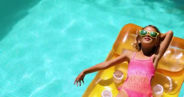 Little girl in sunglasses relaxing in swimming pool, enjoying suntans, swims on inflatable yellow mattress — Stock Video
