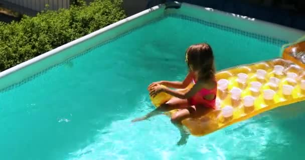 Bambina seduta su materasso giallo gonfiabile e palla da gioco, si diverte in piscina — Video Stock