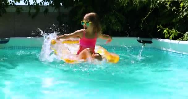 Kleines Mädchen sitzt auf aufblasbarer gelber Matratze und hat Spaß im Schwimmbad — Stockvideo
