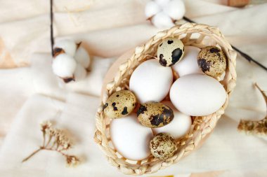 Paskalya yassı kompozisyonu pamuk çiçekleri ve paskalya yumurtaları kumaş arkaplanda küçük bir sepetin içinde yatar. Mutlu Paskalyalar, kopyalama alanı.