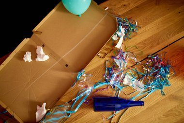 Parti kutlamalarından sonra parti kaosundan sonra parti artıklarını kutlamak için pizza kutusu, boş mavi şişeler, şarap bardağı ve parti süslemeleri olan dağınık ahşap masa..