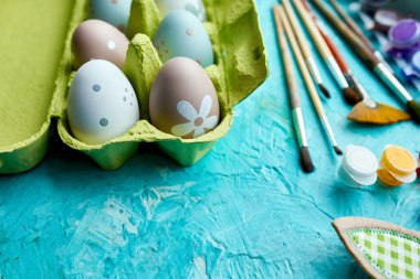 Mavi arka planda fırçalı, boyalı ve dekoratif elementli yumurta paketleri. Uzayı kopyala, Mutlu Paskalyalar, DIY, düz yat.