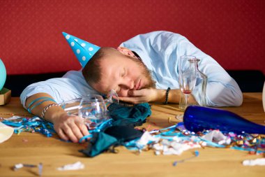 Doğum günü partisinden sonra dağınık odada mavi şapkalı bir adam uyuyor. Evde yorgun bir adam var.