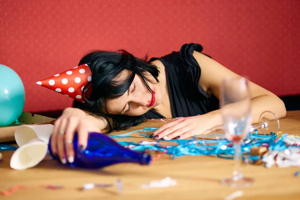 Kırmızı rujlu ve şapkalı genç bir kadın, doğum günü partisinden sonra dağınık bir odada uyuyor, partiden sonra evde yorgun bir kadın.