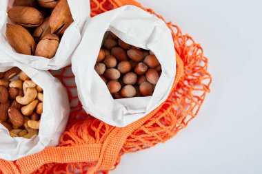 Masadaki çeşitli fındık çeşitlerinin üst görüntüsü alışveriş poşetinde beyaz arka planda, sıfır atık yiyecek alışverişi. Atık olmayan yaşam, fındık teslimatı. Boşluğu kopyala.