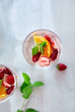 Çilekli, portakallı ve nane şekerli yaz kokteyli beyaz masada, ev yapımı ferahlatıcı limonata, çilekli punç, üst manzara, kopyalama alanı..